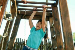 wenig Mädchen spielen auf Spielplatz, hängend auf ein horizontal Bar. aktiv wenig Mädchen ausüben draußen, hängend auf Affe Riegel im das Spielplatz. foto