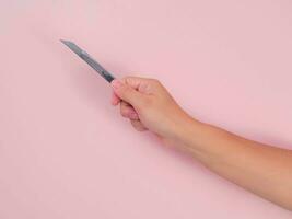 schließen oben von weiblich Hand halten Cutter Messer isoliert auf Rosa Hintergrund. Hand halten ein Silber Cutter mit ein Scharf Klinge im das Vordergrund. foto