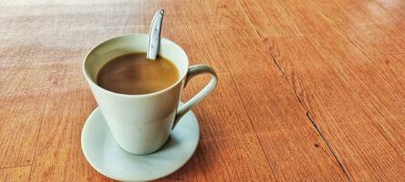 heiß Kaffee im ein Weiß Kaffee Tasse ist platziert auf ein hölzern Tabelle im ein warm und Licht Atmosphäre foto