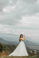 schön Braut gegen das Hintergrund von Herbst Berge im Vorderseite. ein luxuriös Weiß Kleid. Hochzeit Zeremonie auf oben von das Berg. kostenlos Raum. foto