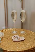 Hochzeit Brille gefüllt mit Champagner auf ein Tabelle bedeckt mit Gold, Nächster zu Gold Hochzeit Ringe auf ein hölzern Stand foto