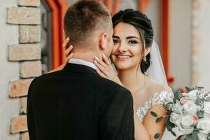 Porträt von das Braut und Bräutigam gegen das Hintergrund von das Fenster von ein alt authentisch Haus, Umarmungen und Küsse. kostenlos Raum. Hochzeit gehen im das Park foto