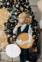 fröhlich Weihnachten und glücklich Feiertage. heiter wenig Junge in der Nähe von das Weihnachten Baum mit Weihnachten die Geschenke. Kinder sind haben Spaß. liebend Familie mit Geschenke im das Zimmer. foto