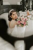 Porträt von ein jung Mädchen von das zurück, mit schön Haar und bilden im ein luxuriös Hochzeit Kleid auf das Schritte von ein Restaurant in der Nähe von Rose Blumen. Vertikale Foto. foto