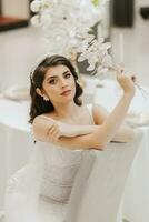 Porträt von ein schön Mädchen im ein Hochzeit Kleid. das Braut im ein luxuriös Kleid, Sitzung auf ein Stuhl. Vertikale Foto