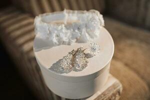 ein Weiß Hochzeit Bein Band und elegant Kristall Ohrringe Stand auf ein Weiß runden Korb. Geschenk Kasten. Hochzeit Einzelheiten foto