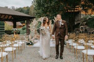 Bräutigam und Braut auf das Hintergrund von das Hochzeit Bogen. Jungvermählten mit ein Hochzeit Strauß, Gehen nach das Hochzeit Zeremonie, dekoriert mit Blumen und getrocknet Blumen im das öffnen Luft. foto