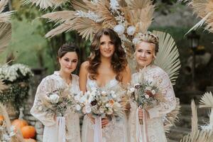 ein Foto von das Braut und ihr Freundinnen halten identisch Blumensträuße gegen das Hintergrund von das Hochzeit Bogen