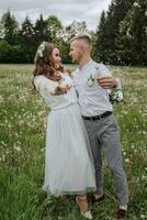 das Braut und Bräutigam gehen im das Feld auf ihr Hochzeit Tag und Schlag Löwenzahn in das Kamera foto