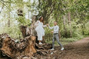 Hochzeit gehen im das Wald. das Bräutigam hält das Braut Hand und Sie Stand auf ein groß Baum Stumpf. Vertikale Foto
