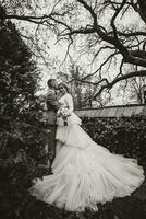in voller Länge Porträt von das Braut und Bräutigam im das Garten in der Nähe von hoch Bäume. Hochzeit gehen im das Garten. schwarz und Weiß Foto