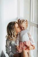 Studio Porträt von ein schön schwanger jung Frau in der Nähe von das Fenster mit ihr Tochter. foto