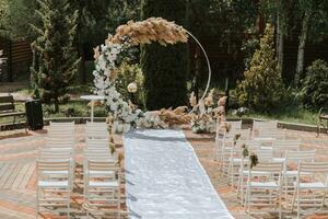 das Hochzeit Bogen im das Park ist gemacht von frisch Blumen und trocken Schilf. Weg Hochzeit Zeremonie. Weiß Stühle zum das Zeremonie foto