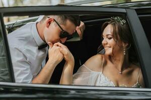 Hochzeit Porträt, Foto von ein stilvoll Bräutigam im ein Weiß Hemd und Bogen Krawatte und ein Brünette Braut mit ein Strauß von Blumen in der Nähe von ein schwarz Wagen.