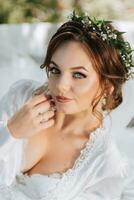 Porträt von ein verträumt Braut Lügen auf ein Bett im ein Garten unter ein Baum. das Braut ist tragen ein Weiß Kleid und ein Tiara von frisch Blumen auf ihr Kopf foto