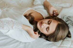 schön jung Braut im ein Weiß peignoir Lügen auf das Bett im seine Schlafzimmer. zuletzt Vorbereitungen zum das Hochzeit. das Braut ist warten zum das Bräutigam. Morgen, das Braut. foto