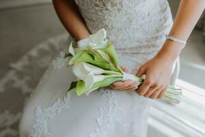 das Braut hält ein schön Hochzeit Strauß von Weiß Calla Blumen. Weiß Abend Kleid, schön Schmuck auf ihr Hand foto