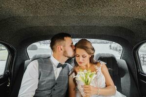 jung glücklich Braut und Bräutigam im ihr Auto jubeln und Kuss nach das Hochzeit Zeremonie foto