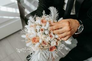 Hochzeit Strauß von Rosa Rosen, Gefieder und getrocknet Blumen im das Hände von das Bräutigam, Nahansicht foto