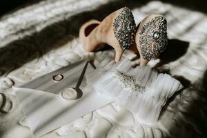 Hochzeit Schuhe von das Braut auf ein hoch Hacke von Beige Farbe mit Steine über das Hacke, ein Briefumschlag mit ein Hochzeit Gelübde und ein Hochzeit Ring von das Braut ist Stehen Nächster zu es foto
