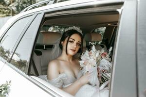 das Braut sitzt im ein Weiß Luxus Auto auf das Hochzeit Tag mit ein Strauß. Porträt von das Braut. üppig Weiß Spitze Kleid. foto