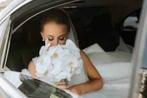 ein blond Braut, lächelnd aufrichtig, sitzt im ein schwarz Auto auf ihr Hochzeit Tag. Porträt von das Braut. schön bilden und Haar. ein luxuriös Weiß Kleid foto