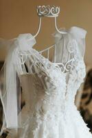 ein exquisit Hochzeit Kleid mit ein Schleier auf das Schultern, Stehen auf ein Mannequin im das Braut Zimmer. das Kleid ist dekoriert mit Perlen und gestickt mit Blumen. Hochzeit Einzelheiten. foto