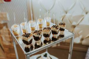 ein köstlich Hochzeit. Weiß Kuchen dekoriert mit Blumen. Süßigkeiten Bar zum ein Bankett. Feier Konzept. modisch Nachspeisen. Tabelle mit Süßigkeiten, Süßigkeiten. Früchte foto