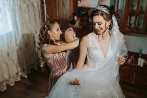 Porträt von das Braut mit ihr Freunde. das Braut freunde befestigen das Braut Kleid. Brünetten öffnen Schultern. foto