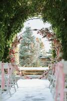 das Hochzeit Bogen im das Park ist gemacht von frisch Blumen und trocken Schilf. draussen Hochzeit Zeremonie im Natur im ein Grün Gang. Weiß Stühle zum das Zeremonie foto