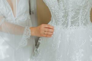 Weiß Hochzeit Kleid auf ein Mannequin im das Zimmer, Nahansicht von das Braut Hand auf das Mannequin. Hochzeit Einzelheiten, modern Hochzeit Kleid mit lange Zug, lange Ärmel und öffnen zurück foto