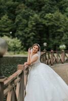 Hochzeit Porträt. das Braut im ein Weiß Kleid auf das Brücke mit ein fließend Schleier. aufrichtig lächeln. Wind und Schleier. Diadem. foto