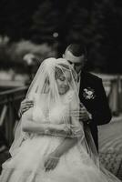 Hochzeit Porträt. das Braut im ein Weiß Kleid auf das Brücke mit ein fließend Schleier, das Bräutigam ist Stehen hinter ihr. aufrichtig lächeln. Wind und Schleier. Diadem. foto