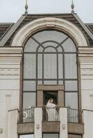 Braut auf das Balkon von das Hotel im ein Weiß Kleid mit ein Schleier, kostenlos Raum, Vertikale Foto. auf Ihre Hochzeit Tag foto