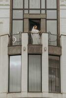 Braut auf das Balkon von das Hotel im ein Weiß Kleid mit ein Schleier, kostenlos Raum, Vertikale Foto. auf Ihre Hochzeit Tag foto