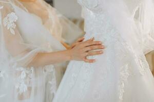 ein schön Mädchen mit ein Hochzeit Frisur im ein transparent Kleid ist vorbereiten zum ein Hochzeit im ein Hotel mit ein königlich Innere. das Braut posiert Nächster zu ihr Hochzeit Kleid auf ein Mannequin foto