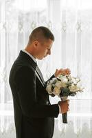 stilvoll Bräutigam mit ein Strauß von Blumen im ein Hotel Zimmer. Bräutigam Morgen. das Bräutigam ist bekommen bereit im das Morgen Vor das Hochzeit Zeremonie foto
