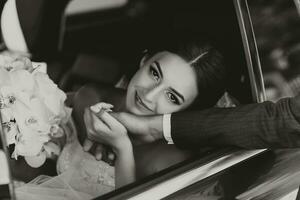 Nahansicht Porträt von ein ziemlich schüchtern Braut im ein Auto Fenster, halten ihr Bräutigam Hand und suchen beim das Kamera foto