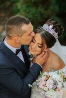 Porträt von glücklich Hochzeit Paar, Braut und Bräutigam im Herbst Wald, Park posieren in der Nähe von Stein Stufen. ein Mann im ein Anzug, ein Mädchen im ein Hochzeit Kleid. Bräutigam Küsse seine Freundin. Foto von über