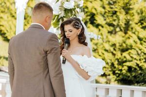 empfindlich Zeremonie von das Braut und Bräutigam. ein glücklich frisch verheiratet Paar ist Stehen gegen das Hintergrund von ein Hochzeit Bogen, sie sagt Ja zu ihn. Hochzeit Gelübde. das emotional Teil von das Hochzeit foto