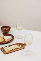 zwei Brille von Weiß Wein, Käse und Cracker auf Weiß Tabelle foto
