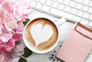 Home-Office-Schreibtisch-Arbeitsplatz mit rosa Hortensienblumenstrauß, Tasse Kaffee und Tastatur foto