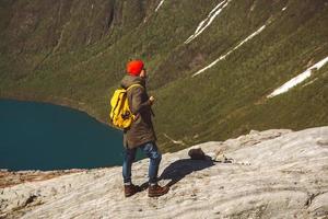 Mann mit einem Rucksack, der auf einem Felsen vor dem Hintergrund von Berg und See steht