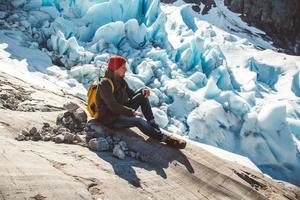 Mann mit Rucksack sitzt auf einem Felsen auf dem Hintergrund eines Gletschers und Schnee