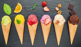 verschiedene Eissorten in Zapfen Blaubeere, Limette, Pistazie, Mandel, Orange, Schokolade, Vanille und Kaffee auf dunklem Steinhintergrund. Sommer und süßes Menükonzept foto