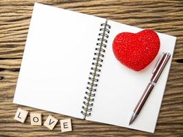 Draufsicht auf Notizbuch und Stift mit rotem Herzen auf Holzschwarzgrund, Liebeswort im Holzwürfel, Valentinstag