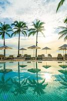 Wunderschöner Luxus-Sonnenschirm und -Stuhl um den Außenpool im Hotel und Resort mit Kokospalme bei Sonnenuntergang oder Sonnenaufgang