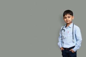süßer kleiner pakistanischer asiatischer Junge trägt weißes Hemd mit Stethoskop, der Doktor spielt, glückliches lustiges kleines Mischrennen-Vorschulkind, das vorgibt, pädiatri foto
