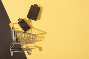 Flacher Miniatur-Supermarktwagen mit Einkaufstüten im schwarzen Freitagsverkauf auf gelbem Hintergrund