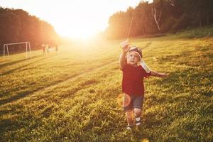 glückliches Kind startet bei Sonnenuntergang einen Drachen auf dem Feld. kleiner Junge und Mädchen im Sommerurlaub foto